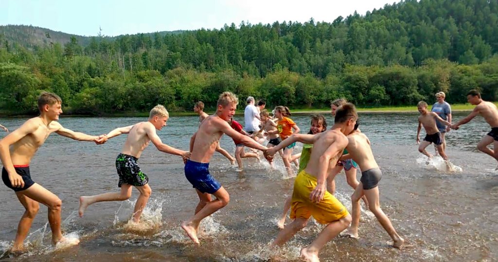 children running and holding hands on a sand bar in a river