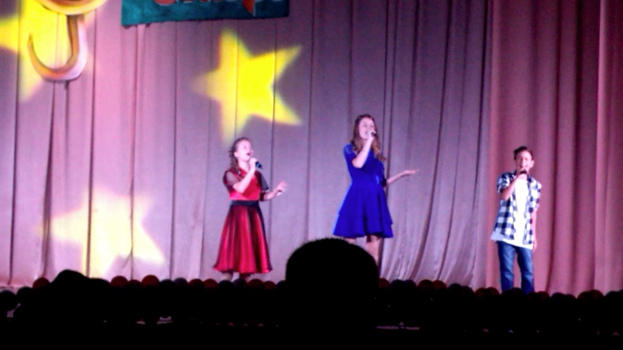 three children singing on stage