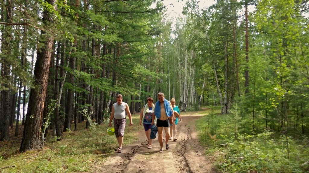 men and women waling in a larch forest next to a lake