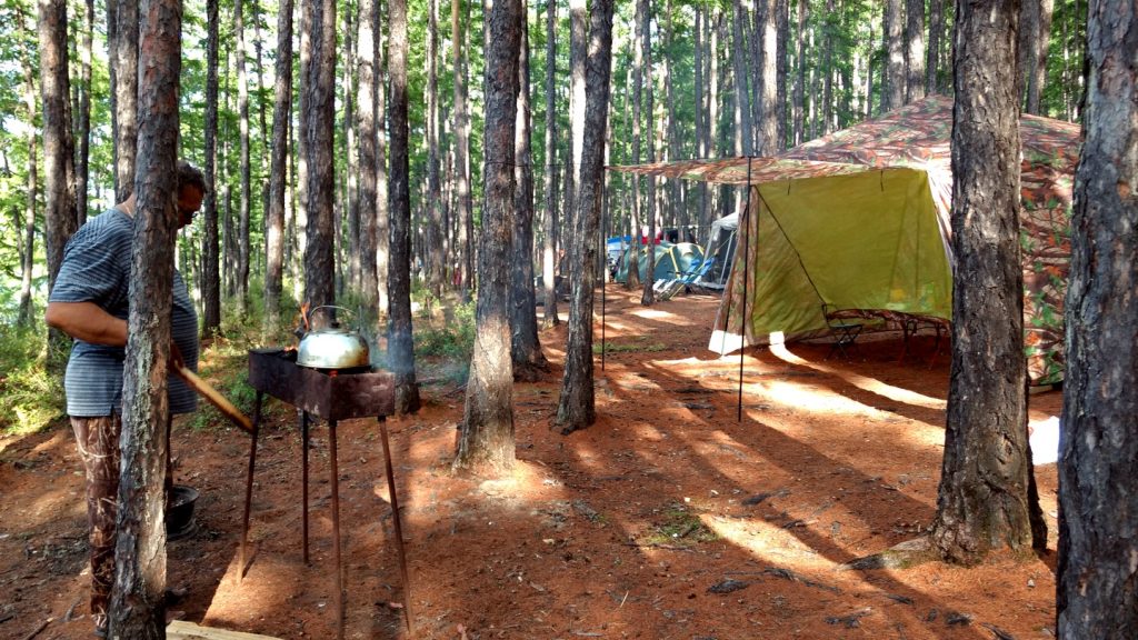 campground with kettle heating on grill, kitchen tent, neighbor tenstie in the background