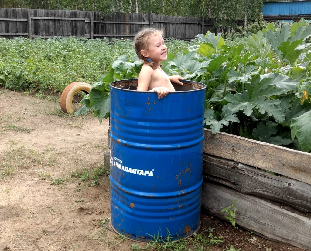 little girl bathing in a water barrel in a big vegetable garden.