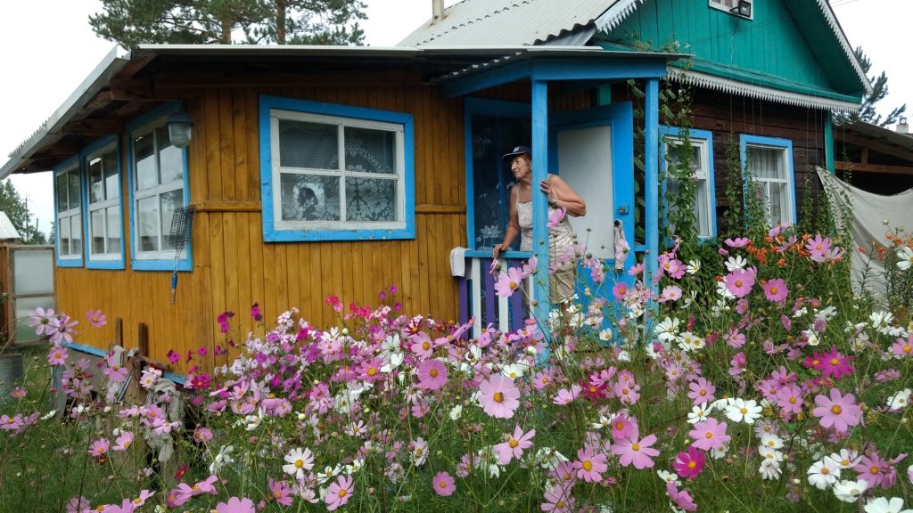 woman at the entrance to a small house with cosmos flowers in front