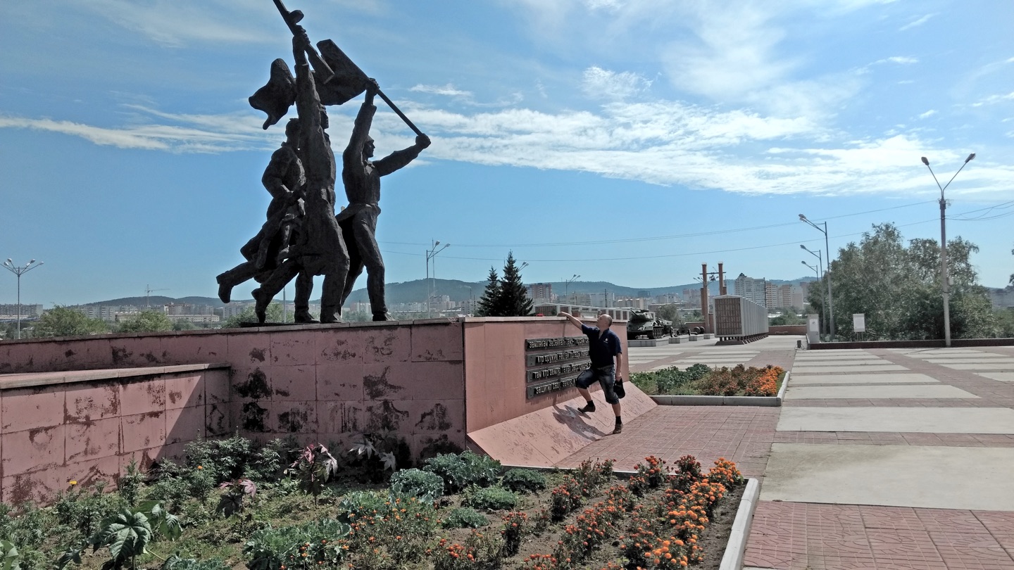 a man leaves flowers on the base of a large statue of three striding soldiers